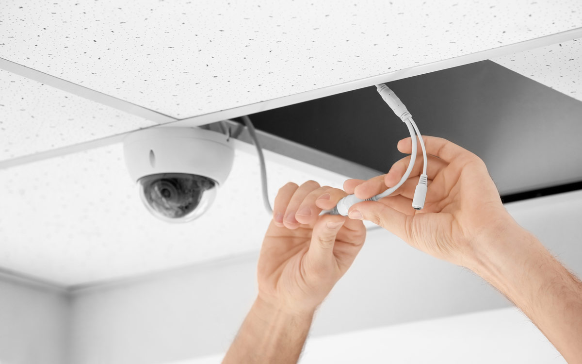 Hands installing a security camera on the ceiling.